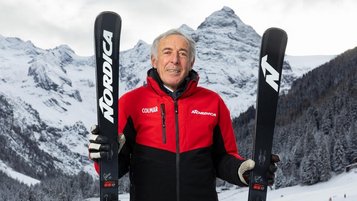 Ein Bild von der Skilegende Gustav Thöni hält in der rechten und linken Hand einen Ski, im Hintergrund die verschneiten Berge rund um das Familienhotel Bella Vista in Südtirol.