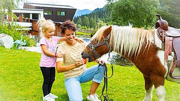 Mutter und Tochter füttern ein Pony im Familienhotel Alphotel Tyrol Wellness & Family Resort in Südtirol.