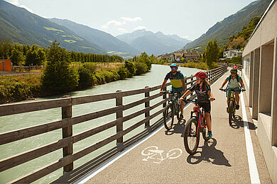 Teenager beim Fahrrad fahren mit der Familie. Die Strecke entlang am Fluss bietet eine tolle Aussicht auf die Berge in Südtirol im Sommer.