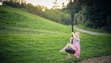 Kleines Mädchen schaukelt auf dem Flying Fox auf dem Außenspielplatz des Familienhotels Schreinerhof im Bayerischen Wald.