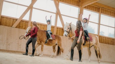 Reiten mit Spaß: Zwei Kinder zeigen stolz ihre Balanceübungen im Familienhotel Friedrichshof.