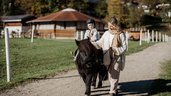 Kleiner Junge sitzt auf dem Pferd und umarmt es im Familienhotel Post Family Resort im Salzburger Land.