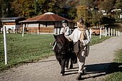 Kleiner Junge sitzt auf dem Pferd und umarmt es im Familienhotel Post Family Resort im Salzburger Land.