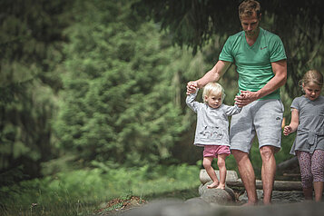 Eine Familie balanciert im Wald über Holzstämme im Familienhotel Alphotel Tyrol Wellness & Family Resort in Südtirol.