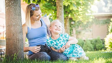 Mutter sitzt mit ihrer Tochter in der Wiese und streichelt mit ihr einen Hasen vom Familienhotel Landgut Furtherwirt in Tirol.