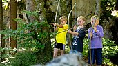 Drei Jungs beim Bogenschiessen mit selbstgebastelten Pfeil und Bogen im Familienhotel Sonne Bezau.