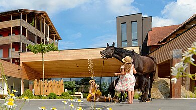 Zwei Mädchen stehen mit einem Pferd vor dem Eingang des Familienhotels Ulrichshof im Sommer.