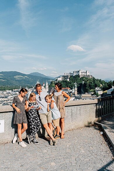 Familie steht in der Salzburger Altstadt, im Hintergrund zu sehen ist die Festung.