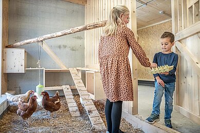 Kinder sammeln Eier im Hühnerstall vom Familienhotel Almfamilyhotel Scherer in Tirol.