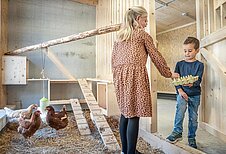 Kinder sammeln Eier im Hühnerstall vom Familienhotel Almfamilyhotel Scherer in Tirol.