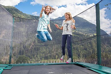 Zwei Mädchen springen auf dem Trampolin draußen auf dem Außengelände des Kinderhotels Sailer in Tirol.