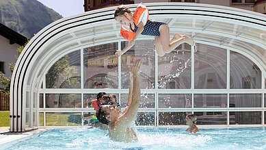 Vater planscht mit seinem Kind im Außenpool des Familienhotels Kaiserhof in Tirol.