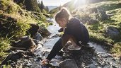 Kind spiel in der Natur am Bach mit dem frischen Bergwasser