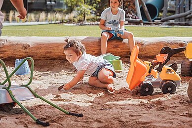 Kind spielt im Sandkasten auf dem Outdoor-Spielplatz des Familienhotels Huber in Südtirol