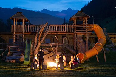 Kinder sitzen in einem Sitzkreis um ein Lagerfeuer mit einem Betreuer im Familienhotel Alphotel Tyrol Wellness & Family Resort in Südtirol.