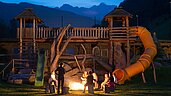 Kinder sitzen in einem Sitzkreis um ein Lagerfeuer mit einem Betreuer im Familienhotel Alphotel Tyrol Wellness & Family Resort in Südtirol.