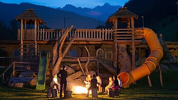 Kinder sitzen in einem Sitzkreis um ein Lagerfeuer mit einem Betreuer im Familienhotel Alphotel Tyrol Wellness & Family Resort in Südtirol.