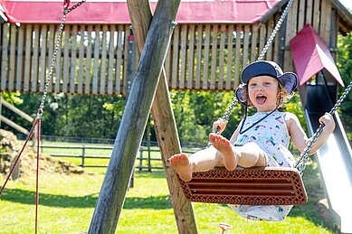 Ein Mädchen schaukelt auf dem Spielplatz des Außengeländes im Landhuus Laurenz.