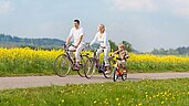 Familie fährt mit dem Fahrrad durch die Rapsfelder an der Ostsee