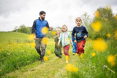 Einige Kinder gehen mit dem Kinderbetreuer durch eine Löwenzahnwiese beim Landhaus zur Ohe im Bayerischen Wald.