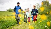 Einige Kinder gehen mit dem Kinderbetreuer durch eine Löwenzahnwiese beim Landhaus zur Ohe im Bayerischen Wald.