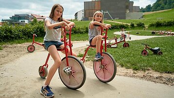 Kinder fahren auf der Rennstrecke des Außenspielgeländes.