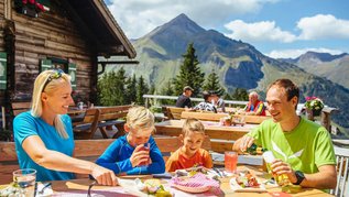 Familie sitzt im Biergarten auf einer Hütte im Salzburger Land und genießt regionale Spezialitäten.