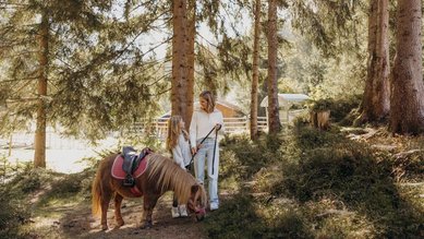 Mutter und Tochter führen Pony durch den Wald beim Familienhotel Habachklause Salzburger Land.