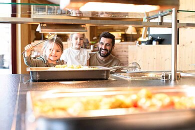 Vater mit zwei Töchtern am Kinderbuffet, Tochter nimmt sich Spaghetti zum Essen.