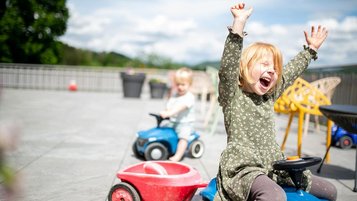 Kinder haben Spaß beim Bobbycar-Fahren auf der Sonnenterrasse des Familienhotels Landhaus zur Ohe im Bayerischen Wald