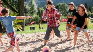 Teens spielen im Sand mit dem Ball auf dem Außengelände des Familienhotel Ramsi in Kärnten