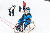 Ein Kind sitzt auf einem Schlitten und wird von seinen Eltern gezogen, diese sind Gäste im Familienhotel Kaiserhof an der Tiroler Zugspitzarena.