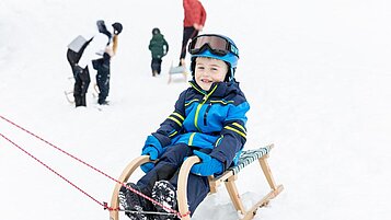 Ein Kind sitzt auf einem Schlitten und wird von seinen Eltern gezogen, diese sind Gäste im Familienhotel Kaiserhof an der Tiroler Zugspitzarena.