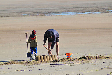 Vater und Sohn bauen am Nordseestrand mit Schaufeln und Eimern eine Sandburg.