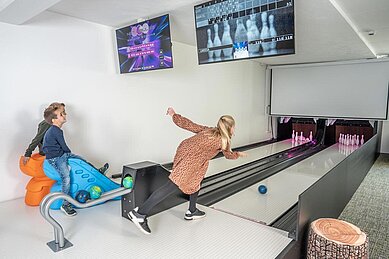 Eine Familie spielt auf der Mini-Bowlingbahn in der Teenslounge im Almfamilyhotel Scherer in Tirol