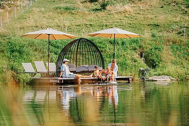 Familie planscht am Ufer des Natur-Badesees auf dem Außengelände vom Familien Resort Petschnighof