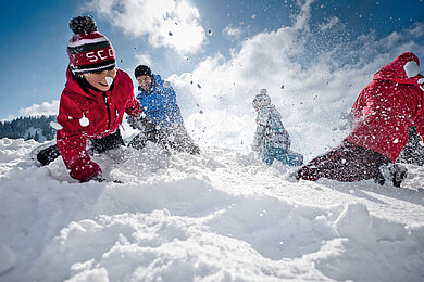 Kinder spielen im Schnee im Winter und haben Spaß. Allgäu bietet sich für jeden Winterurlaub mit der Familie an.