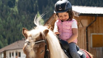 Mädchen sitzt im Reitunterricht im Familienurlaub im Alpenhotel Kindl auf dem Pferd.