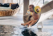 Kleinkind rutscht fröhlich die Wasserrutsche im Indoorpool im Familienhotel Amiamo im Salzburger Land hinunter.