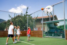 Kinder spielen Basketball auf dem umzäunten Fun-Court des Familienhotels Krone im Allgäu.
