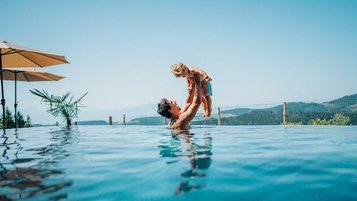 Vater planscht mit seinem Sohn bei sonnigem Wetter im Außenpool des Familienhotels Petschnighof in Kärnten