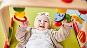 Glückliches Baby spielt mit einem Spielebogen im Babyspielbereich des Familienhotels Aigo welcome family in Oberösterreich.