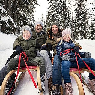 Eine Familie mit zwei Kindern auf Schlitten bei der Abfahrt von einem Berg