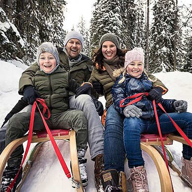 Eine Familie mit zwei Kindern auf Schlitten bei der Abfahrt von einem Berg