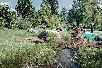 Im Familienhotel Alpenhof Dolomit Family in Südtirol spielen Kinder draußen am Wasser.