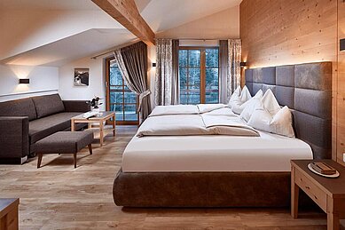 Elternschlafzimmer mit Balkon im obersten Stock Bauernhaus im Hotel Habachklause im Salzburger Land mit einem großen Bett, einer gemütlichen Sitzecke und einem Holzbalkon mit Aussicht auf die Natur.