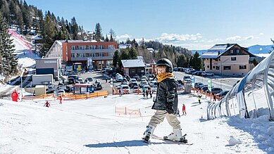 Kind steht auf Skiern auf der Skipiste direkt neben dem Hotel Alpengasthof Hochegger
