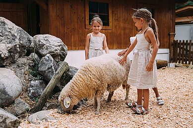 Zwei Mädchen streicheln eine Ziege im Freilaufgehege im Familenhotel Post Family Resort im Salzburger Land.