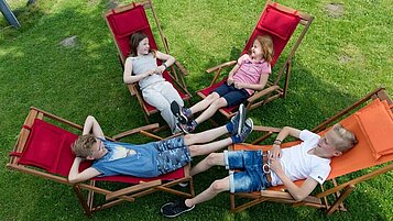 Jugendliche Kinder liegen im Liegestuhl im Garten und Verweilen gemeinsam im Familienhotel Landhuus Laurenz.