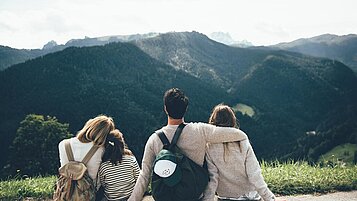 Eine vierköpfige Familie sitzt am Boden eines Weges und blickt in die Berge und durch die wunderschöne Landschaft rund um das Familienhotel Post Family Resort im Salzburger Land.